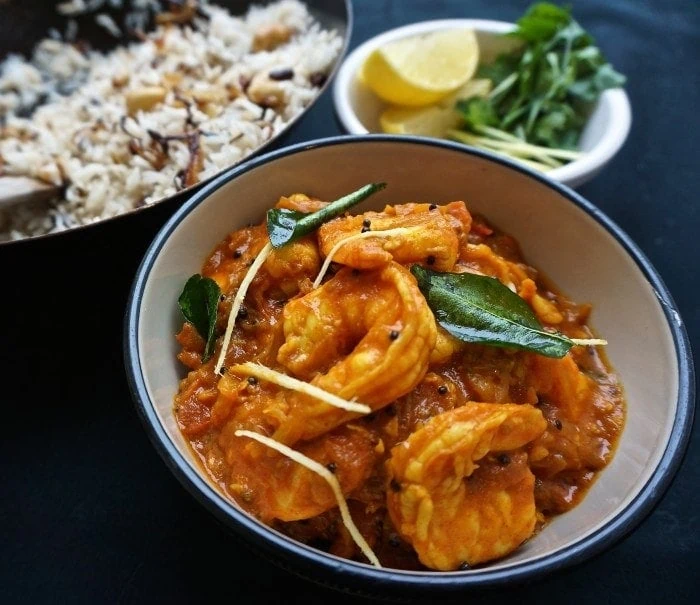 keralan prawn curry garnished with curry leaves in a bowl side with rice and lemons slice