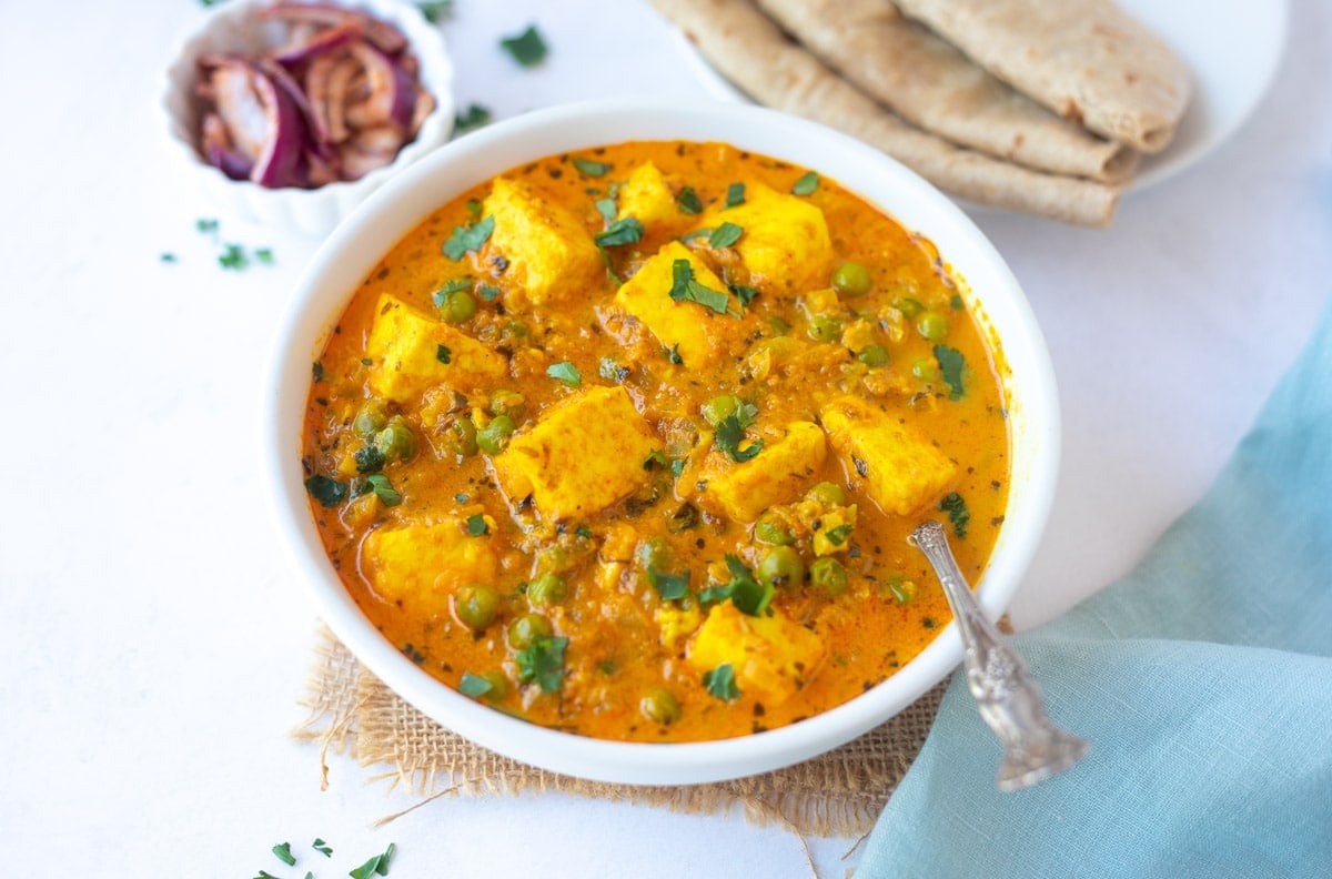 Creamy Matar Paneer served in a bowl with roti and onions on the side