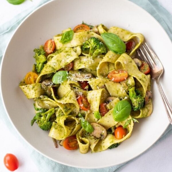 Pappardelle Pesto with Vegetables in a white plate with basil and tomato on side