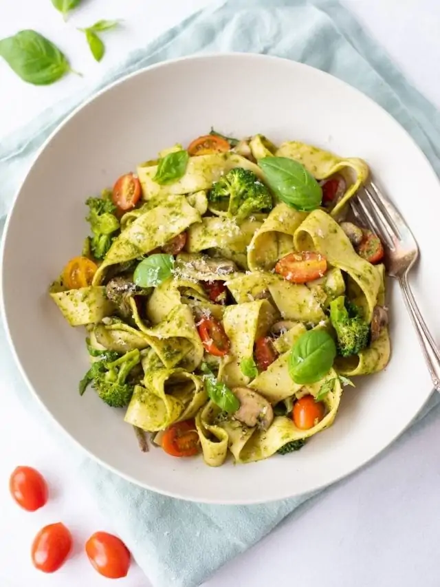 Pappardelle Pesto with Vegetables in a white plate with basil and tomato on side