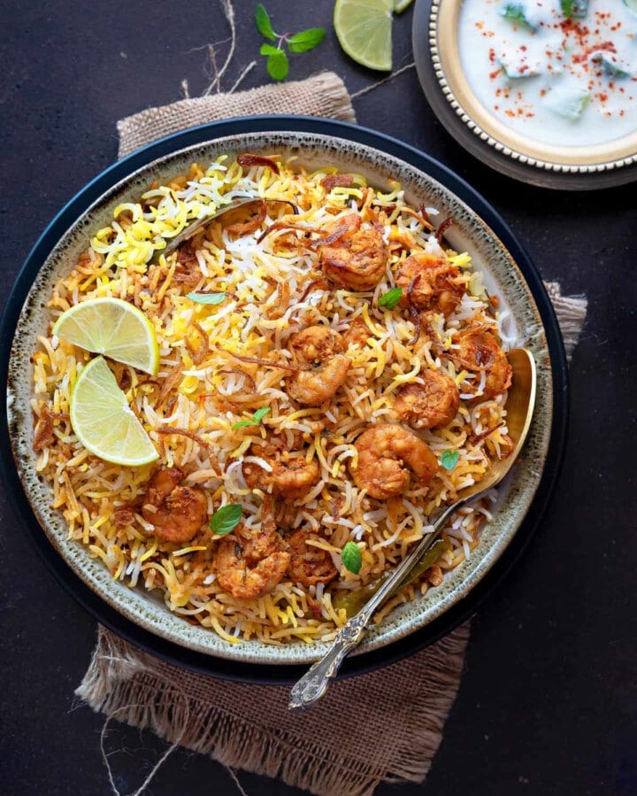prawn biryani in a serving bowl with slice lemon and spoon
