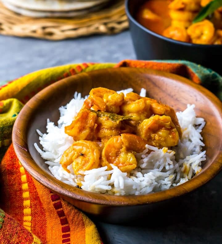 Prawn Gassi (Mangalorean style shrimp curry) served with rice in a wooden bowl. Next to it is a stack of kapparuttis (dosas) and a black bowl with shrimp curry