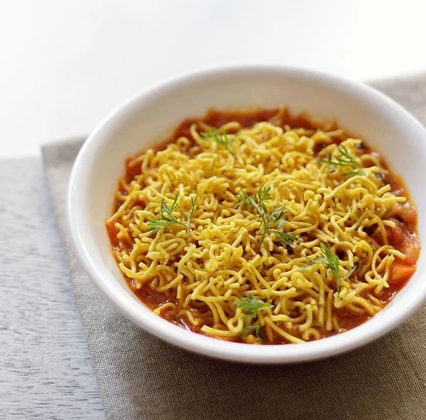 Sev tameta nu shaak garnished with coriander leaves in a white bowl