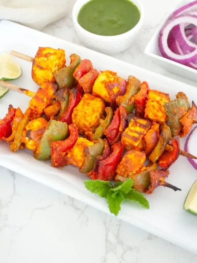 Paneer Tikka in a white plate with cilantro ang lime wedge on side
