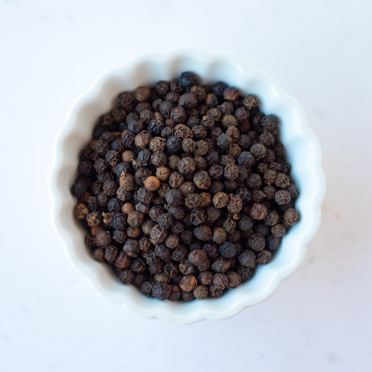 Black whole peppercorns in a white small bowl.
