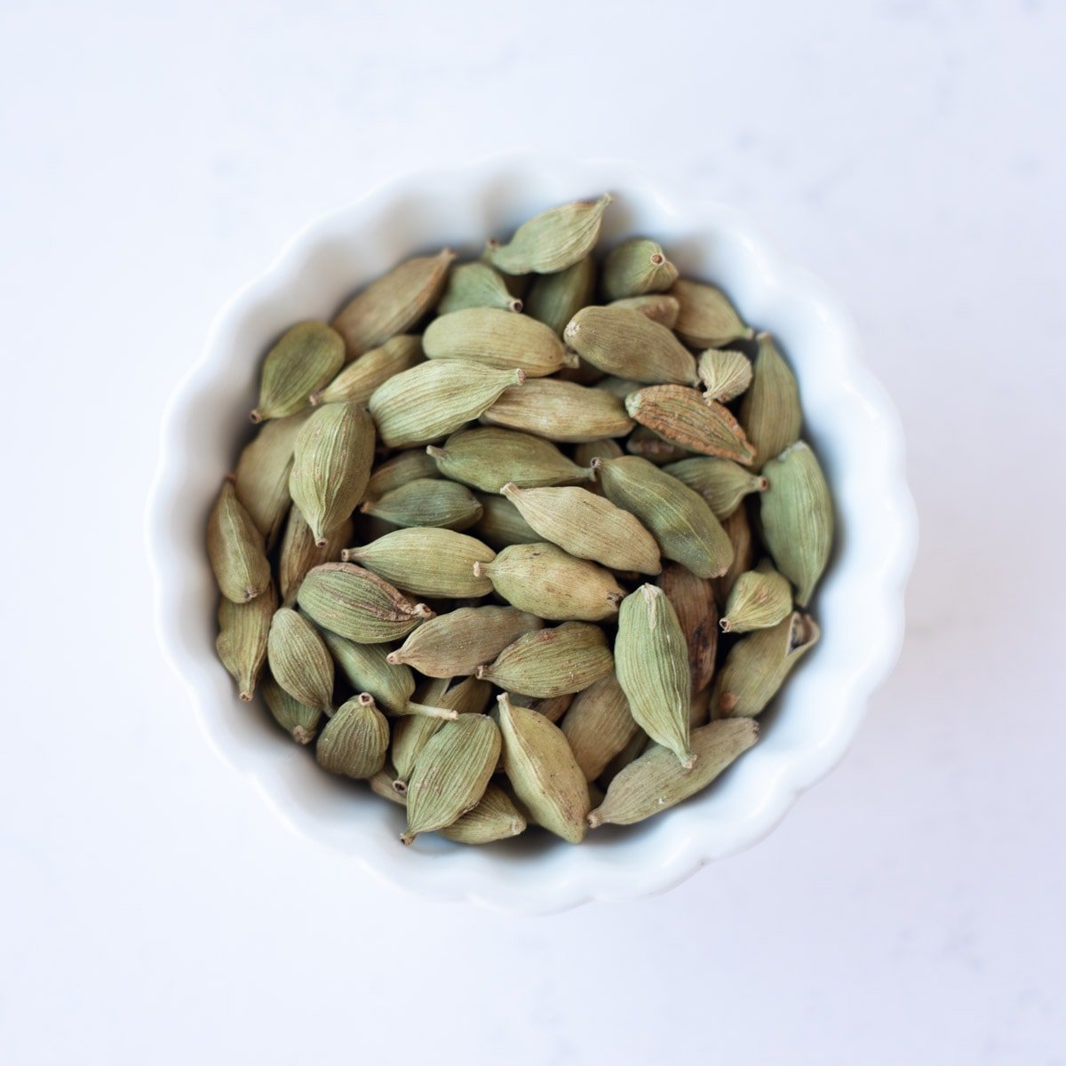 Green cardamom in a small white bowl.