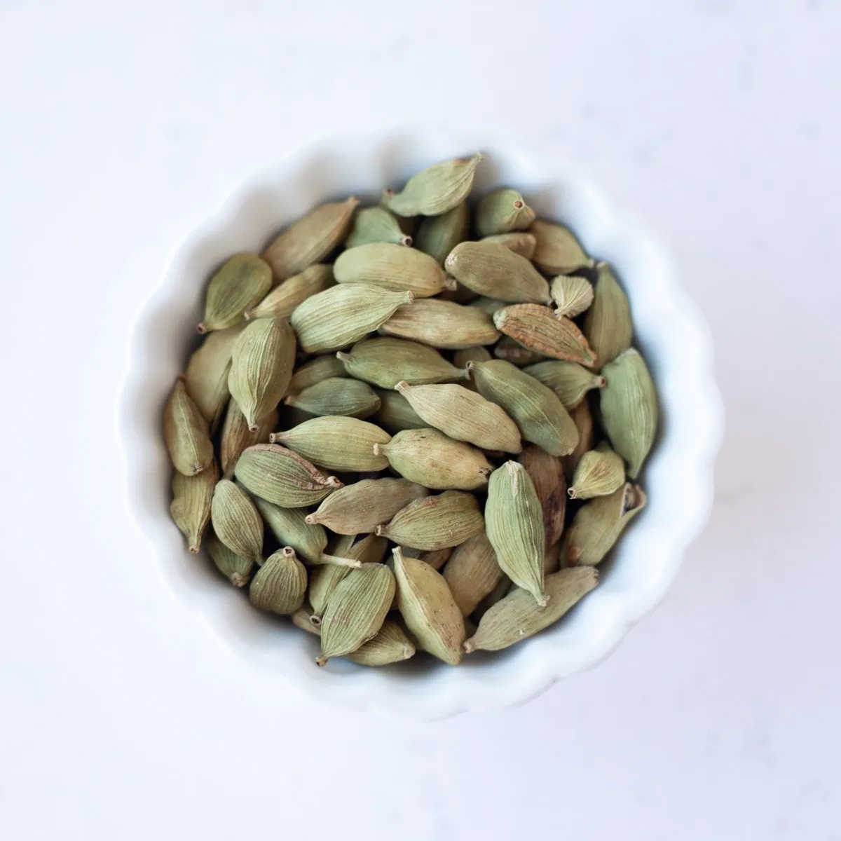 Green cardamom in a small white bowl.
