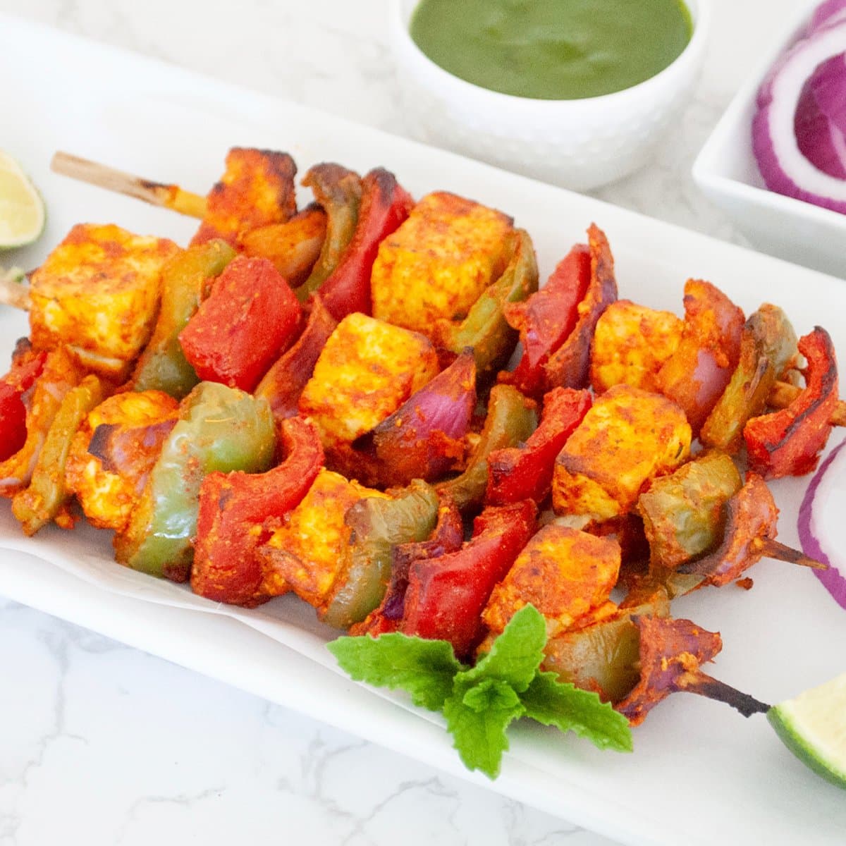 Paneer Tikka in a white plate with cilantro ang lime wedge on side