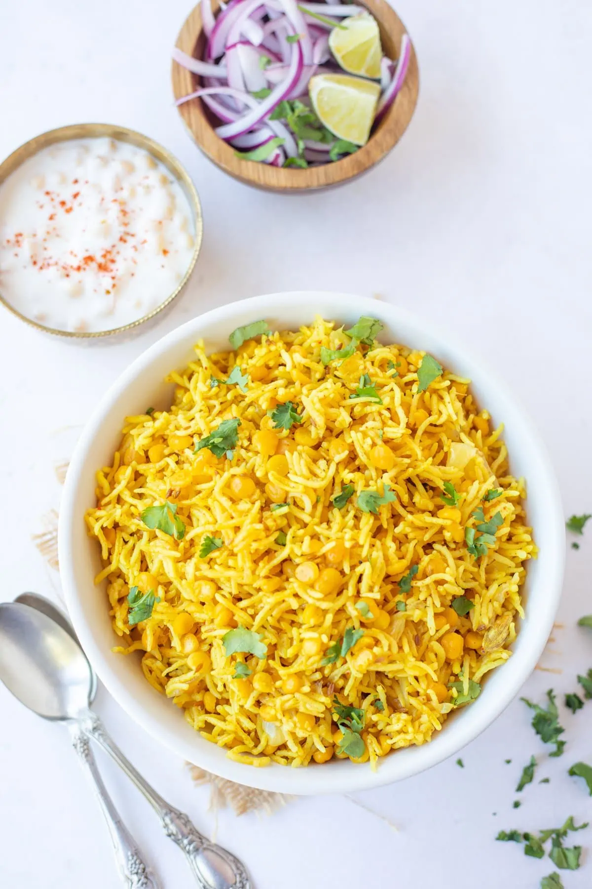 chana dal pulao in a white bowl with raita and onion salad on the side