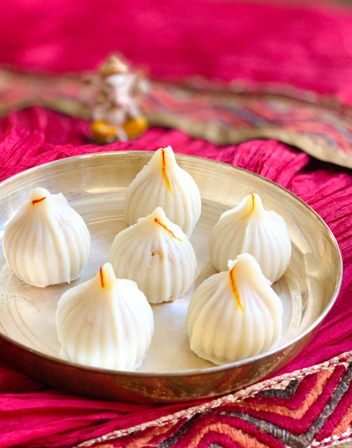 Modak served in a silver plate with Ganesha statue on the back