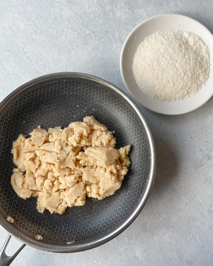 Dough to make coconut almond ladoo in a pan and desiccated coconut in a plate