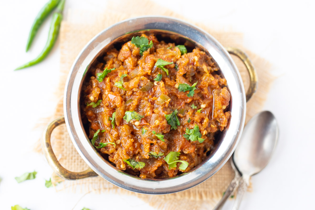 Indian eggplant recipe garnished with cilantro and green chilies on the side