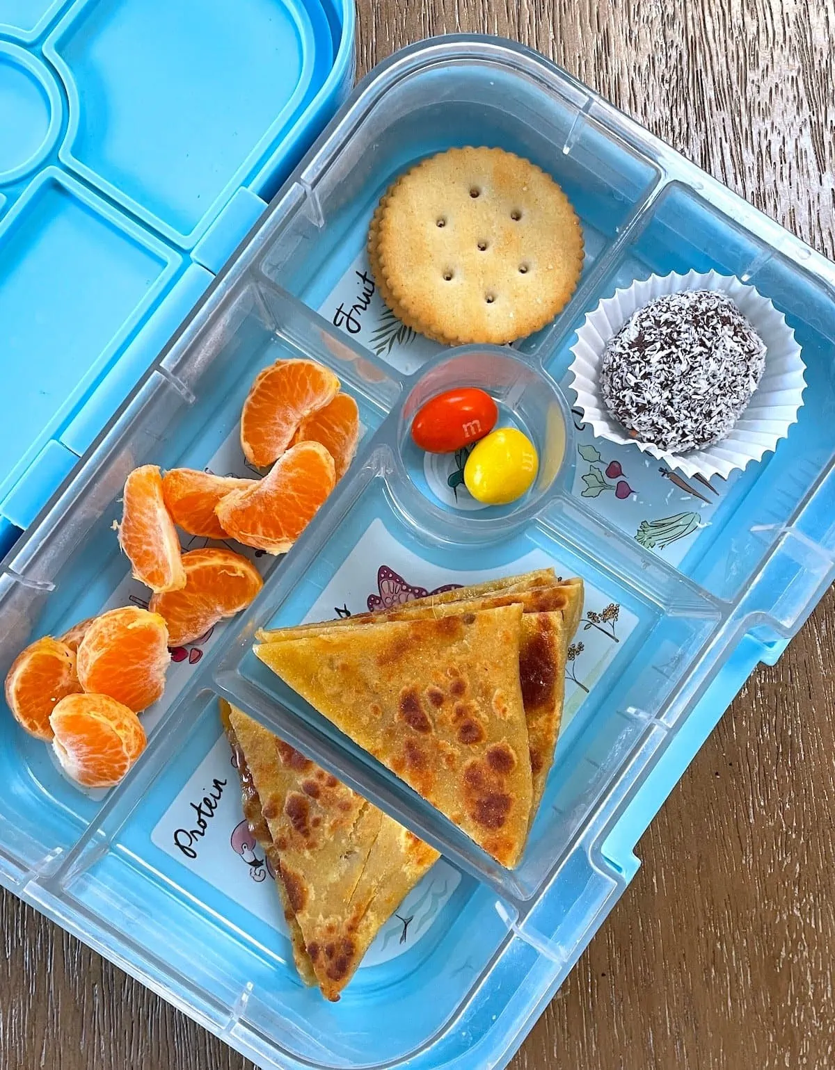 Lunch box with aloo paratha, oranges, and ladoo