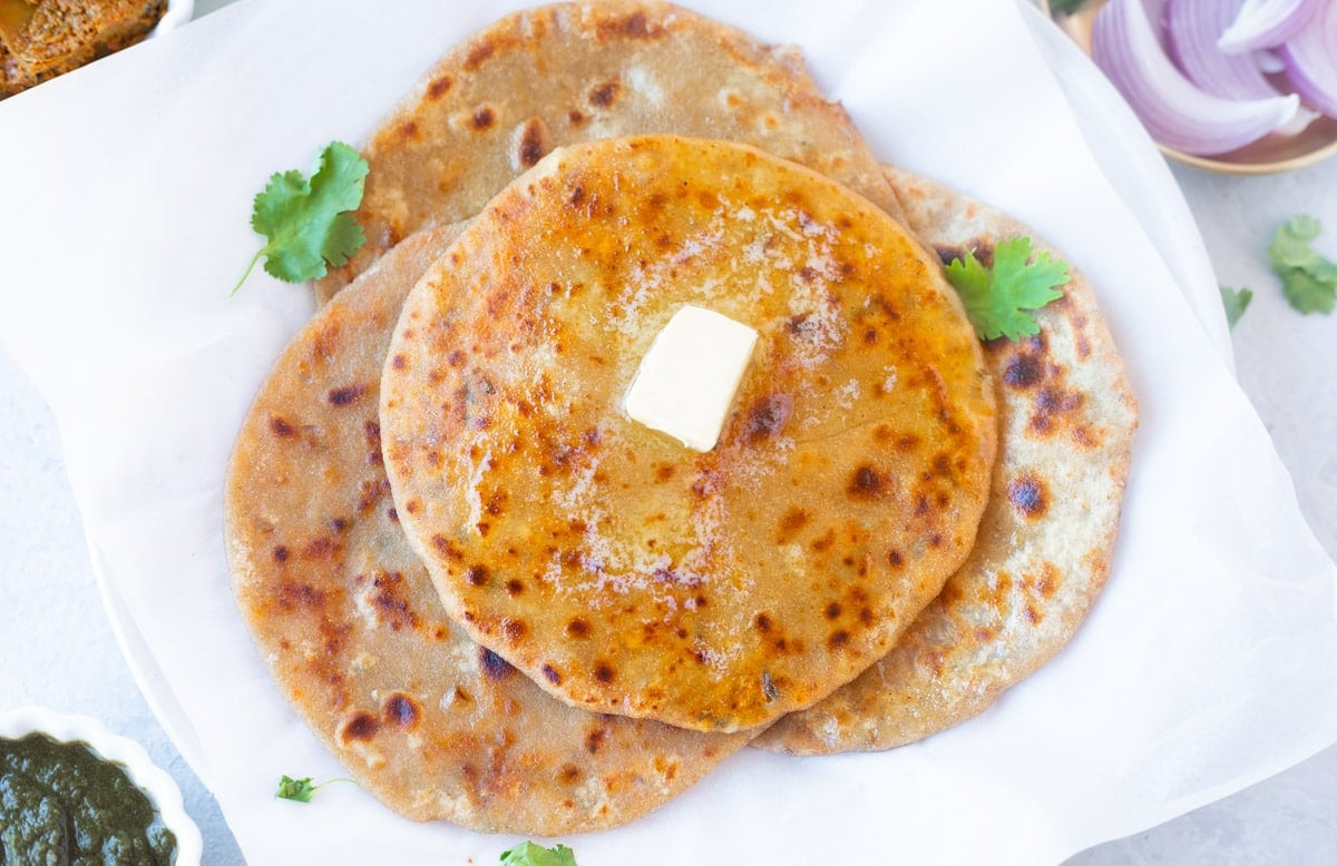 hot paneer paratha in a white plate topped with butter and garnished with cilantro