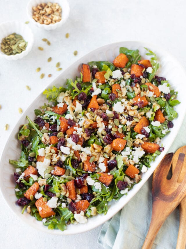 pumpkin salad in a white bowl with mixing spoon on the side