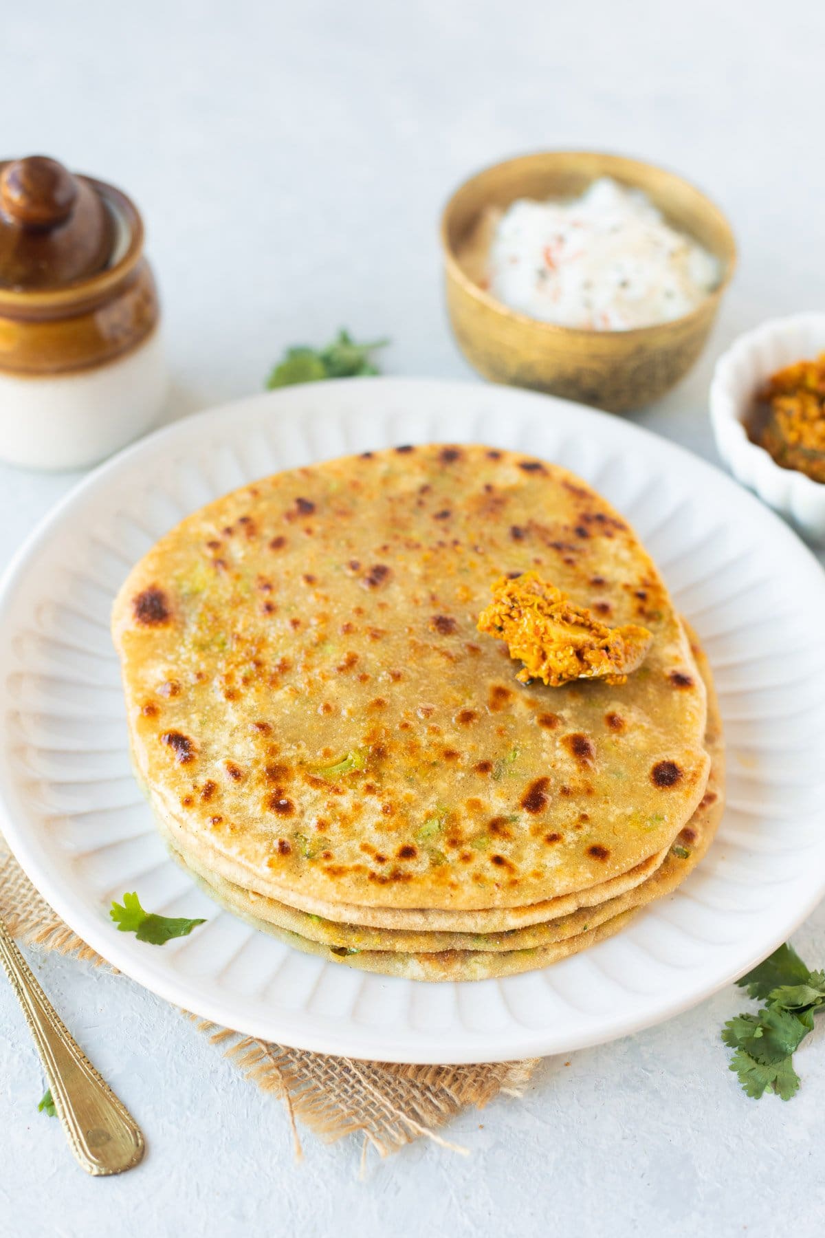 Four broccoli parathas on a white plate with pickle on top