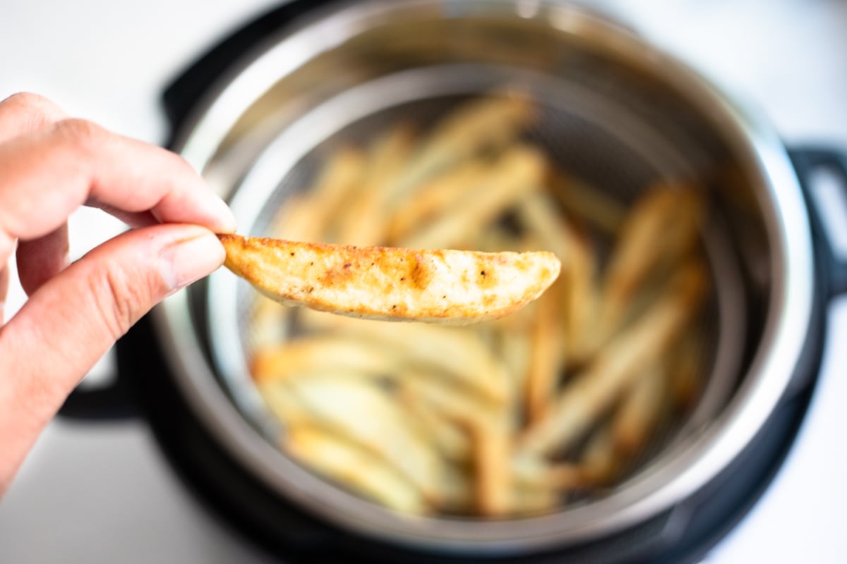a piece of crispy french fry in hand over the instant pot