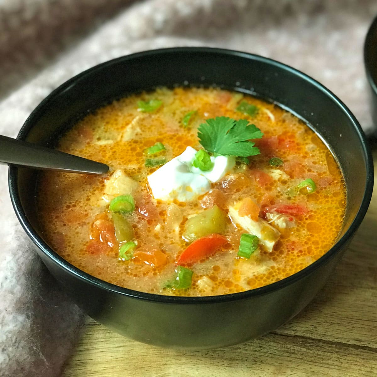 Chicken fajita soup served in a black bowl topped with sour cream