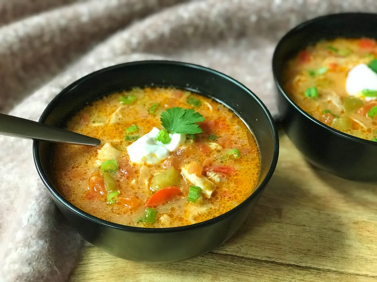 Chicken fajita soup served in two black bowls topped with sour cream and cilantro
