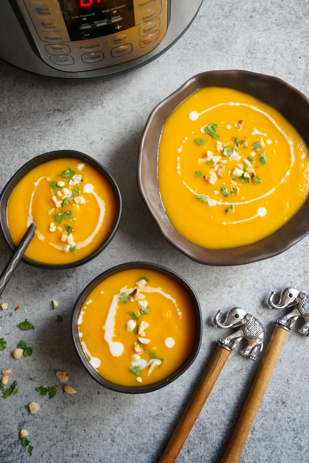 Butternut Squash soup served in 3 bowls in front of the instant pot, garnished with peanuts and cilantro