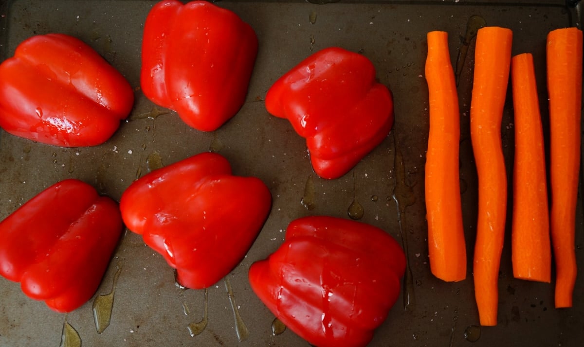 Red bell peppers and carrots on a sheet pan with olive oil to roast