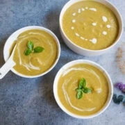 Cream of broccoli soup served in three white bowls garnished with basil leaves.