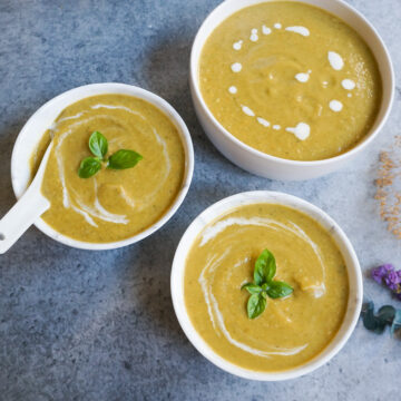 Cream of broccoli soup served in three white bowls garnished with basil leaves.
