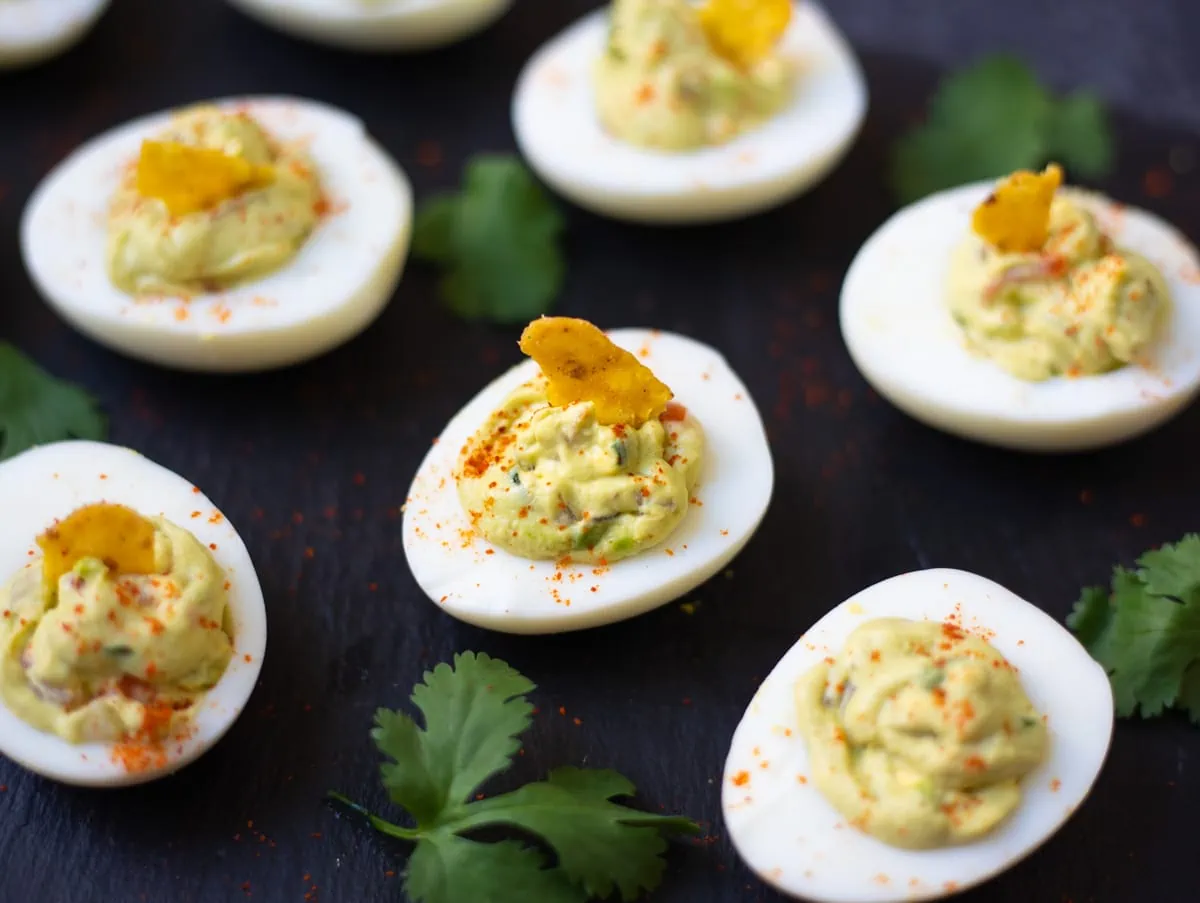 Avocado deviled eggs on a platter with a garnish of cilantro leaves.