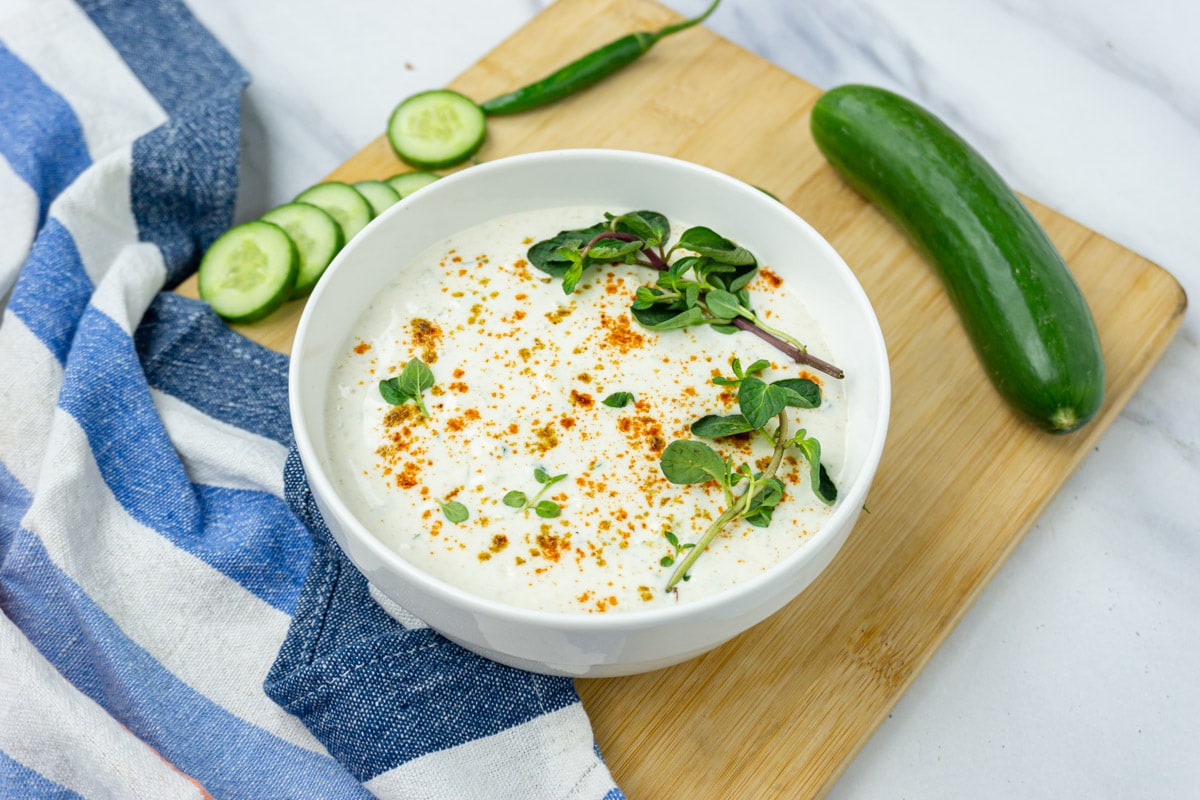 cucumber raita in a white serving bowl on top of a board