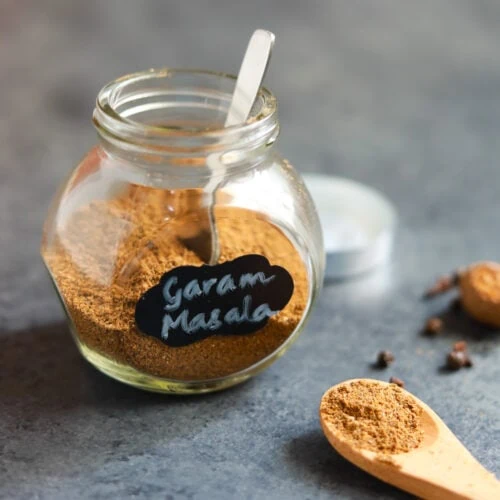 Freshly ground garam masala in a glass container and in a spoon