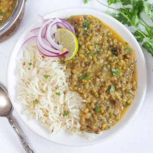 green moong dal in a white plate with onion and lemon