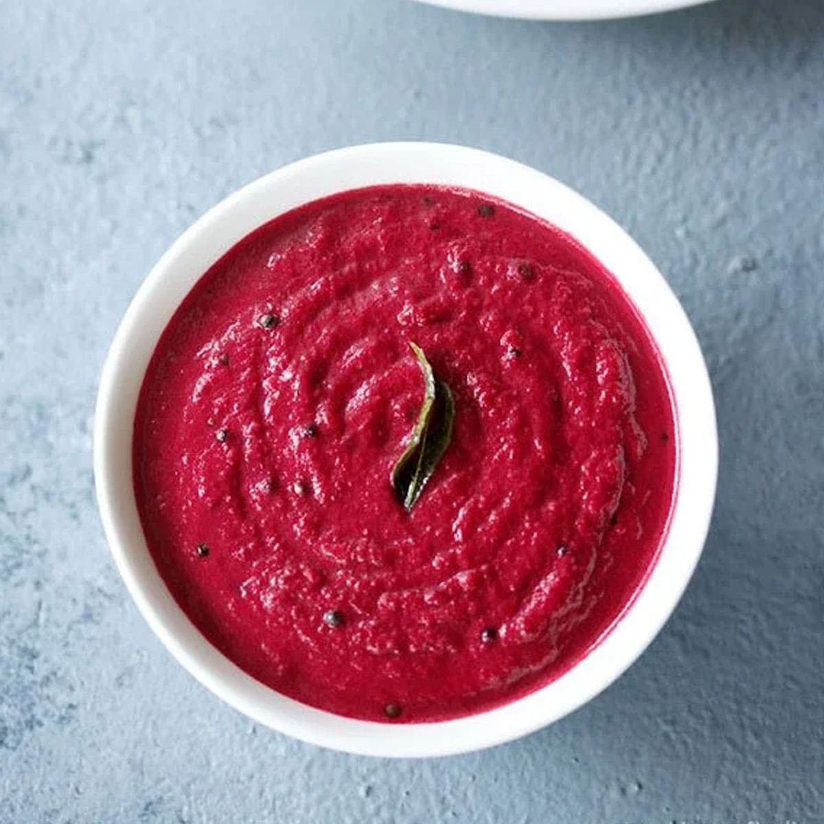 overhead shot of beetroot chutney in white bowl on a light grey blue board.