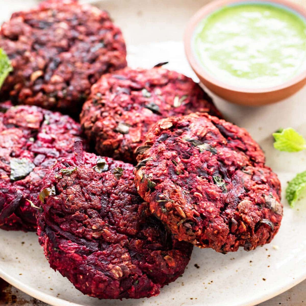 beetroot tikkis arranged on a plate with bowl of chutney on the side