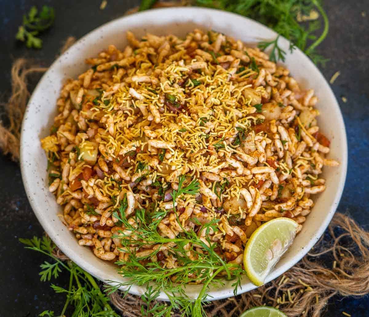 Bhelpuri in a white bowl with lemon slice on the side