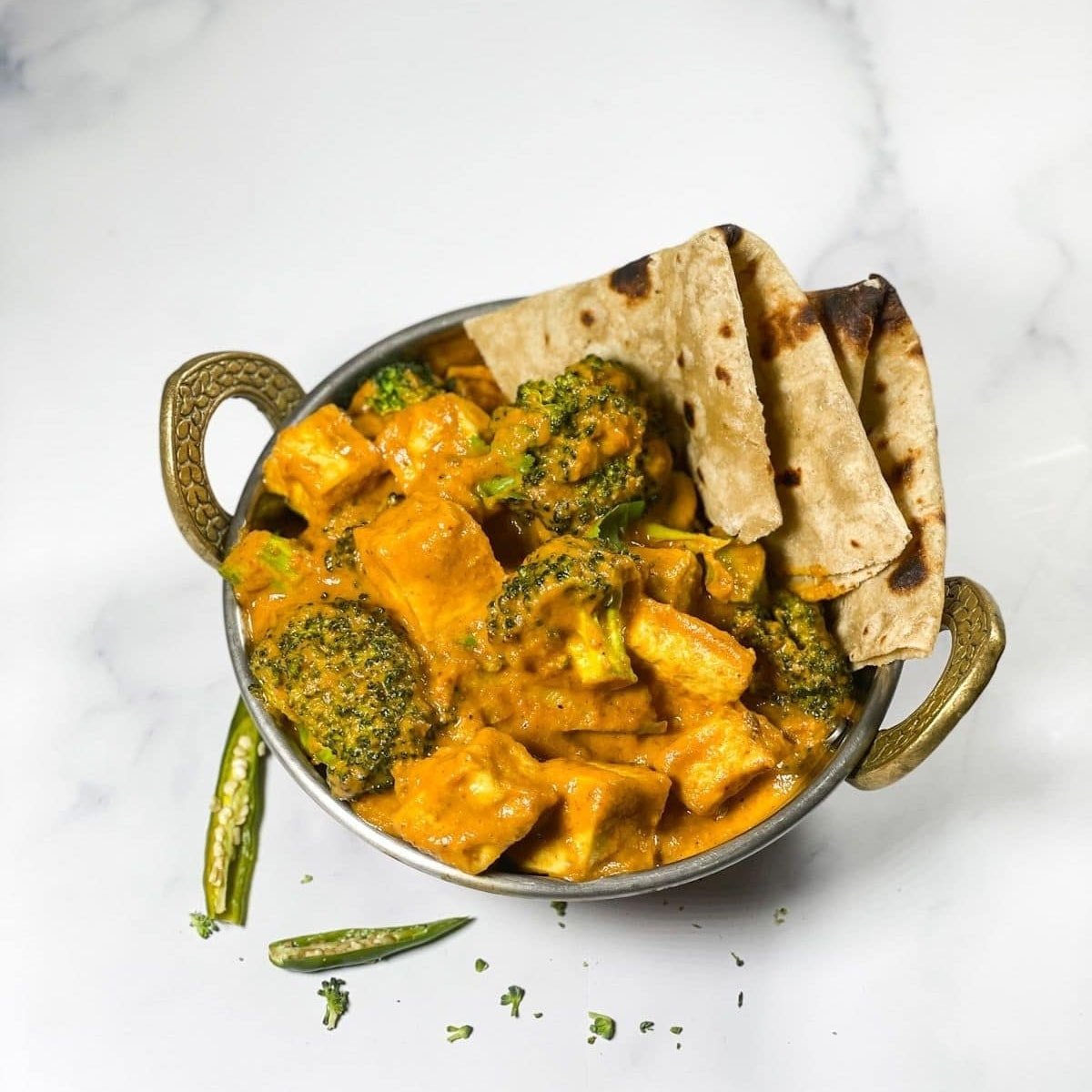 A copper pot is with broccoli tofu curry and roti's.