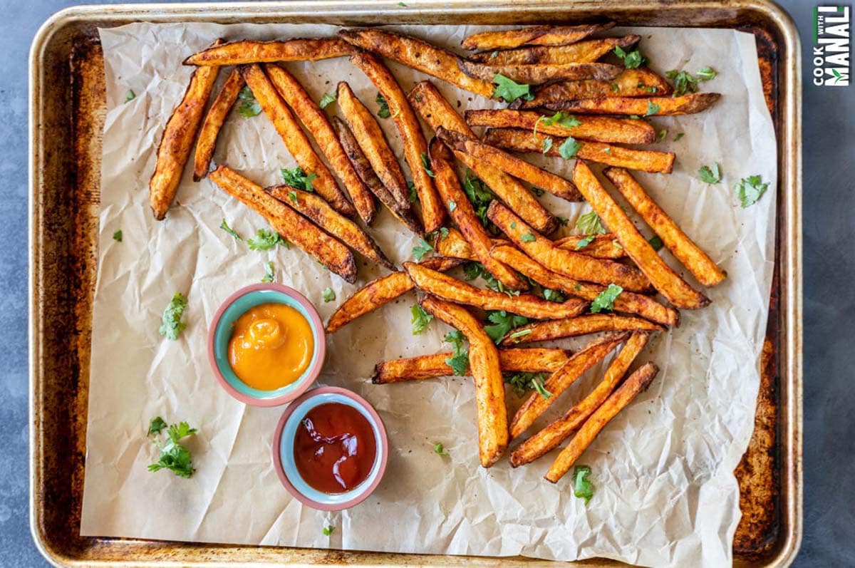 french fries coated with spices placed on a baking tray with 2 bowls of dipping sauces