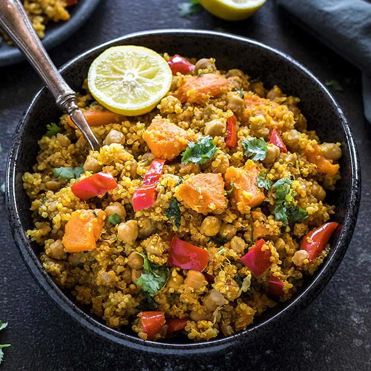 Instant Pot Curried Sweet Potato Chickpea Quinoa in a black bowl and a half cut lemon on the side