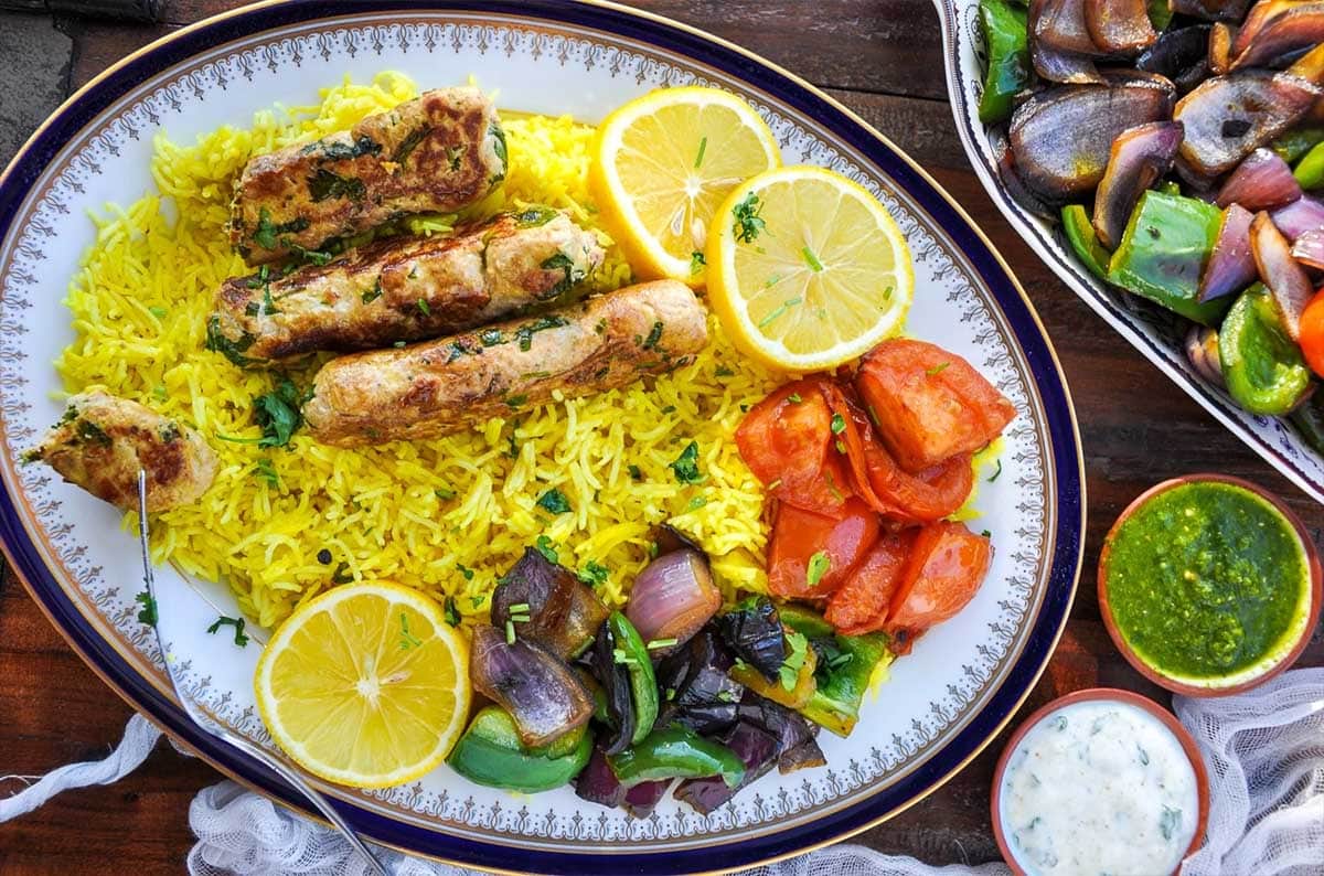 Chicken seekh kebab in a plate with rice, tomato, lime and chili peppers