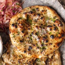 Garlic cheese kulcha served on a plate with pickled onions and boondi raita on the side