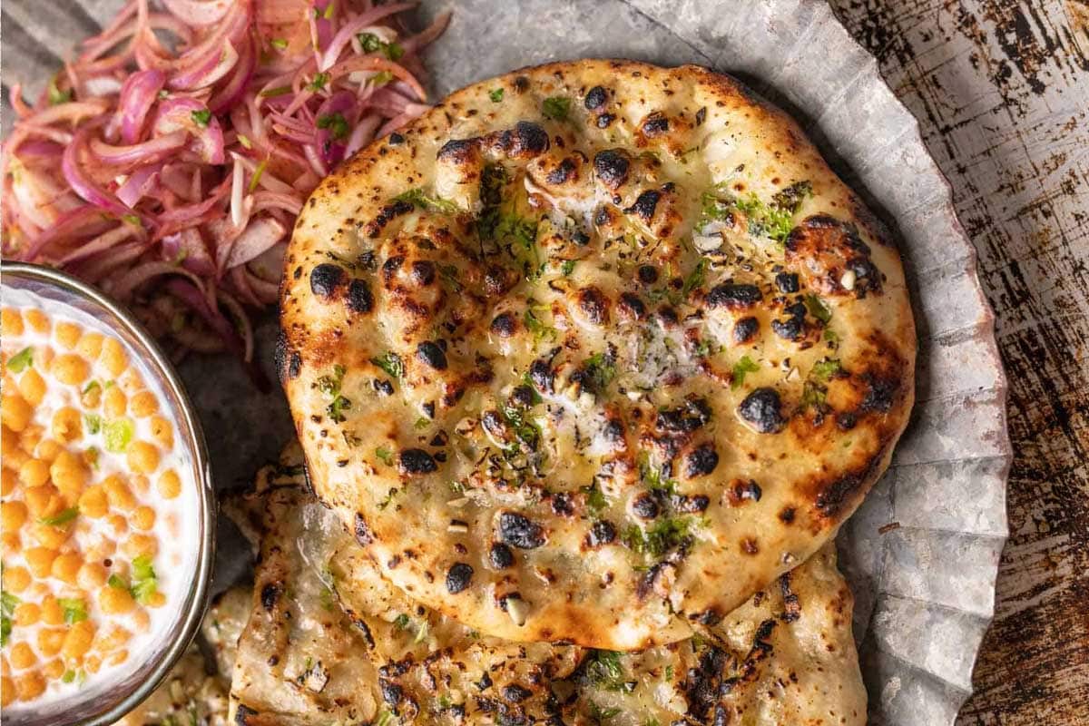 Garlic cheese kulcha served on a plate with pickled onions and boondi raita on the side