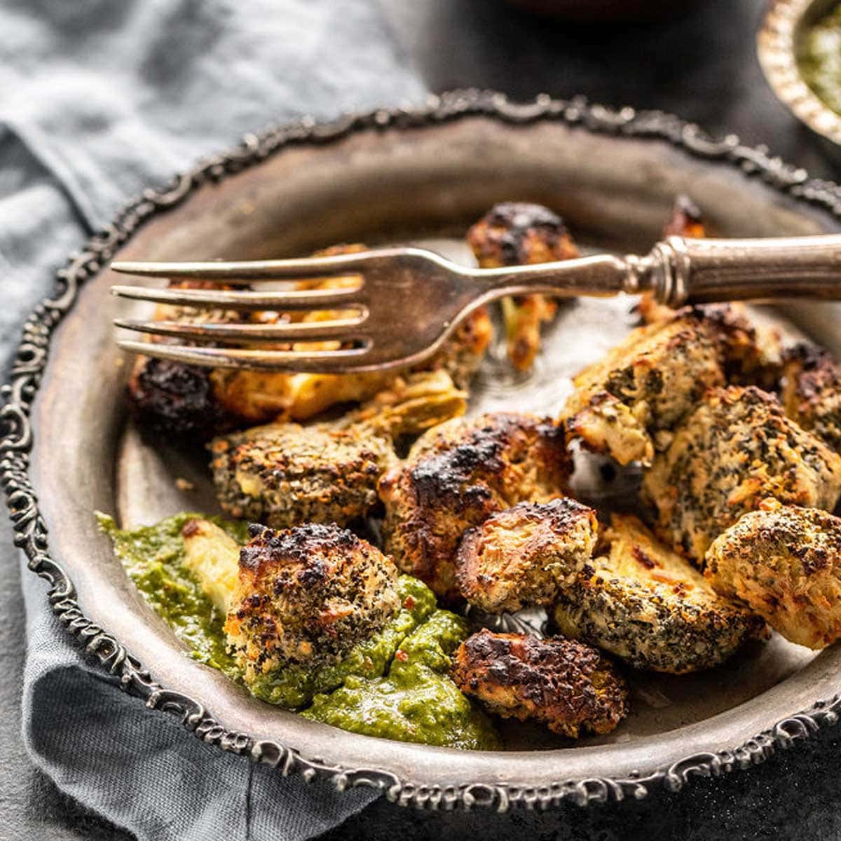 a roasted broccoli floret dipped in cilantro chutney with more roasted broccoli in the plate