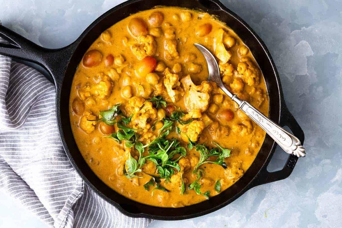 Cauliflower Chickpea Coconut Curry straight from the stove to the table in a cast iron skillet with a spoon