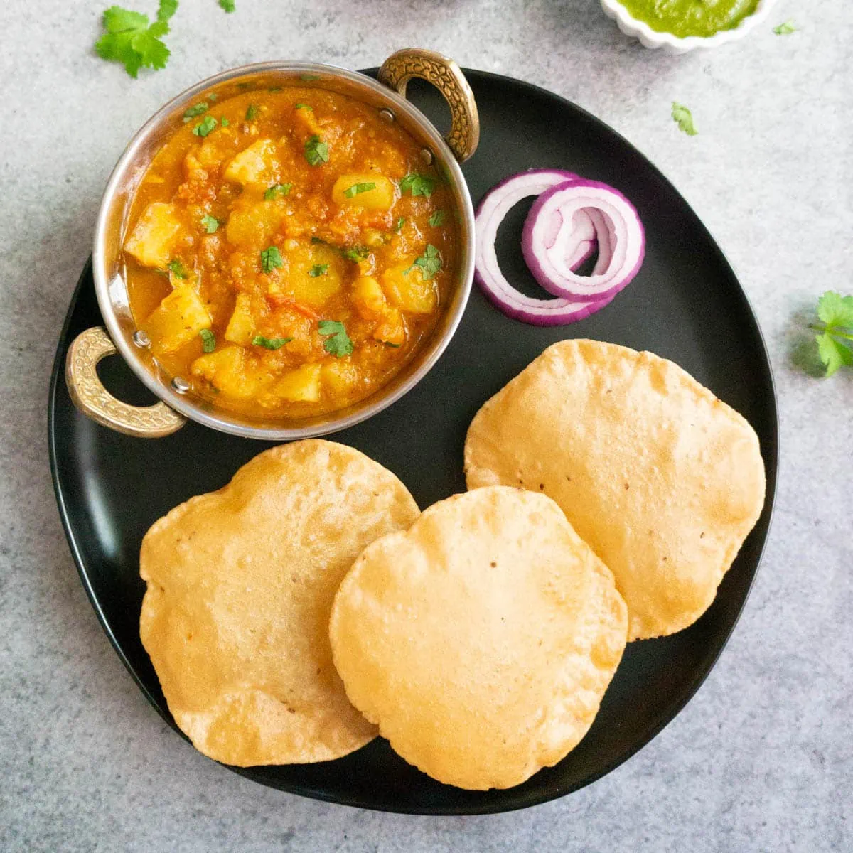 Potato Curry served with puffed Indian flatbread on a plate with red onions.