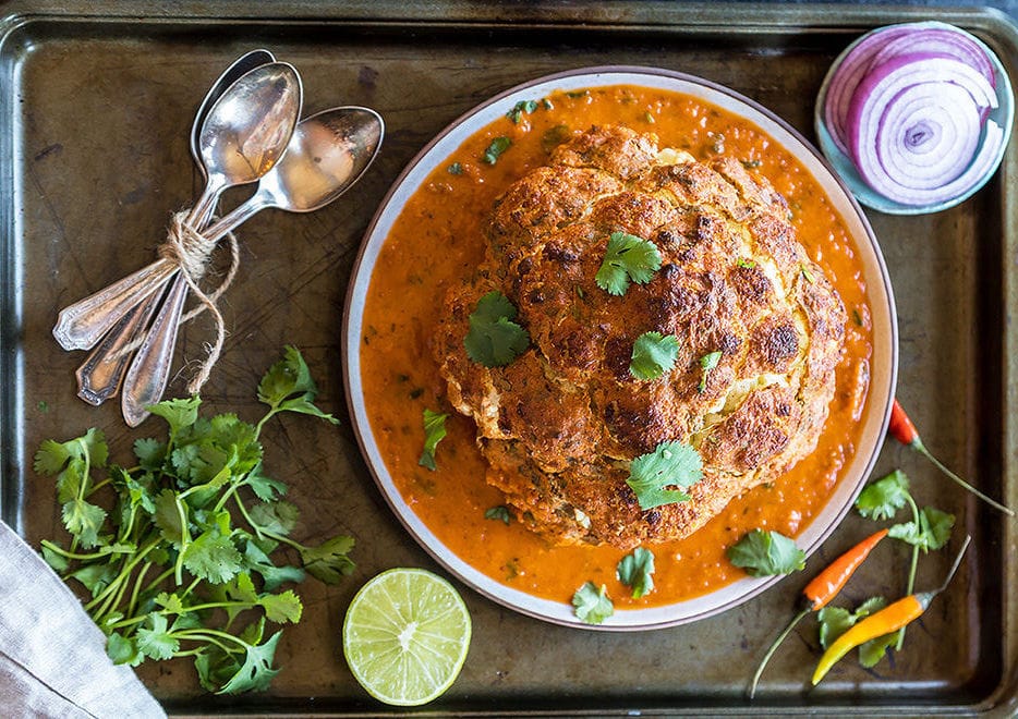 Whole roasted cauliflower in a tray garnished with cilantro 