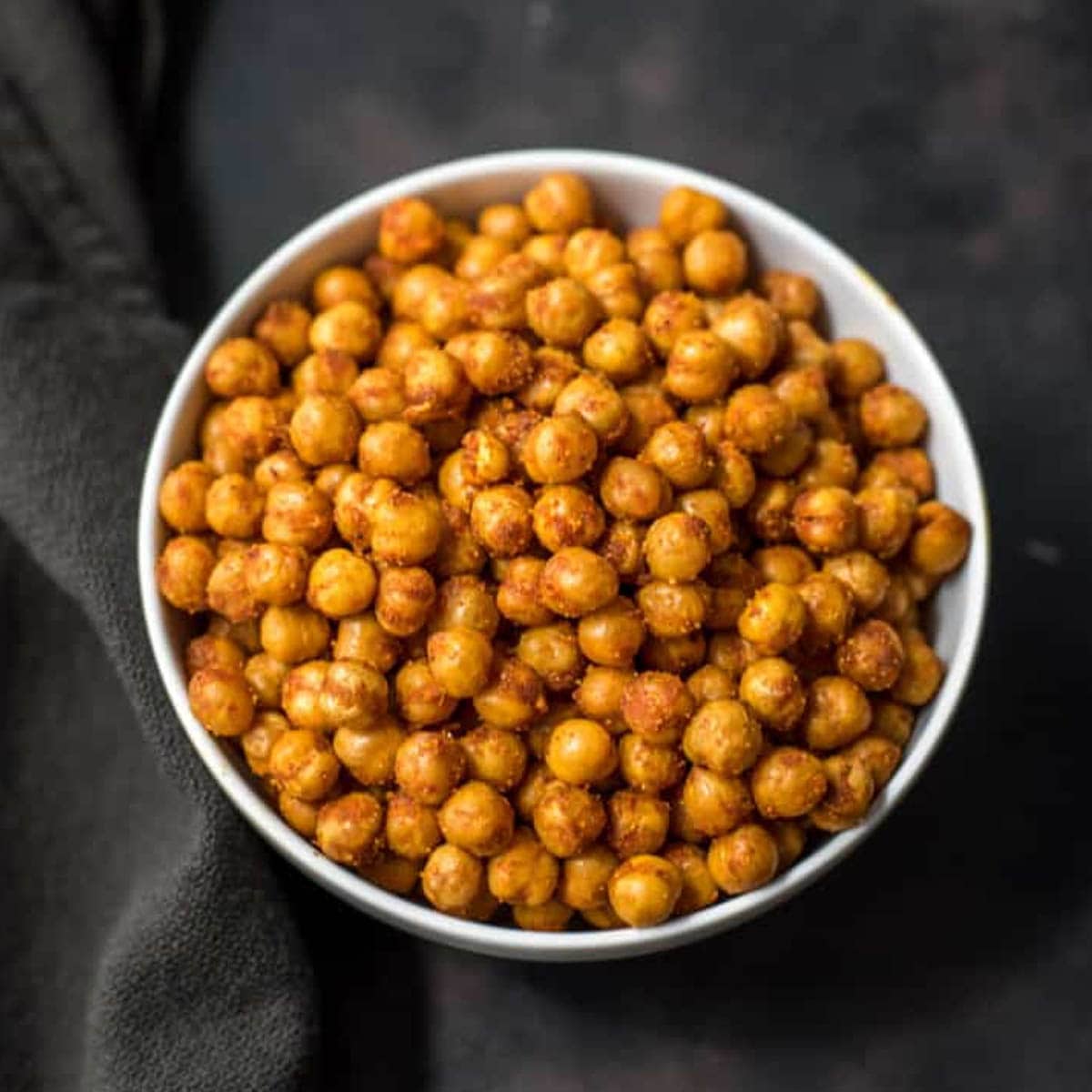 A white bowl with spicy roasted chickpeas on a black towel.