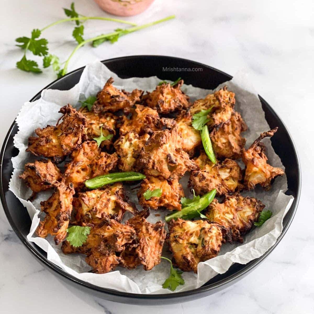 A plate is with air fryer pakora and topped with green chilies and cilantro.