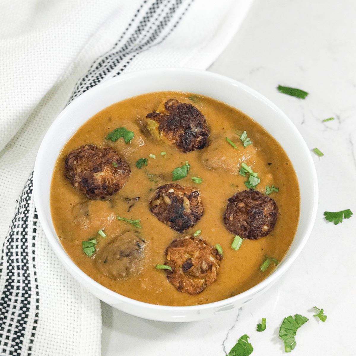 A white bowl filled with gravy and cabbage kofta