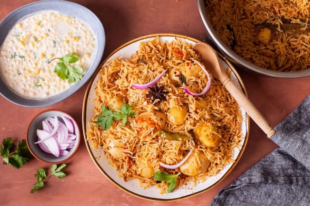 Egg Pulao served in a white plate with bondi raita and sliced onions.