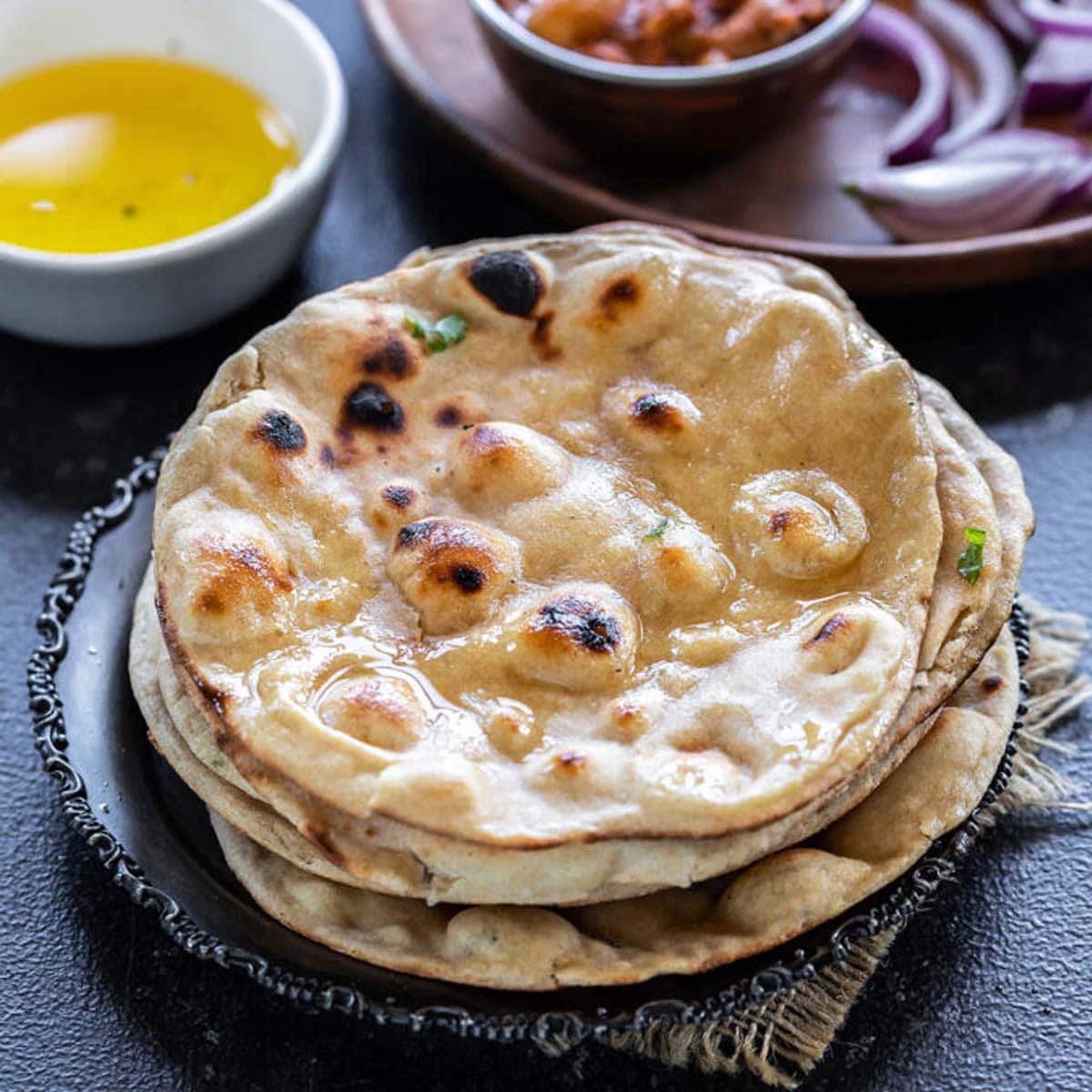 stack on rotis with bowl of ghee and bowl of curry in the background