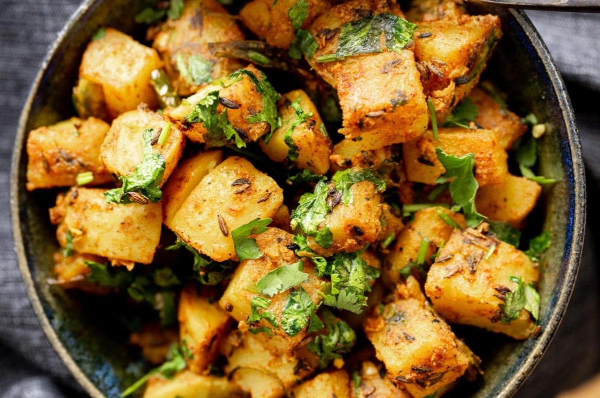 cumin spiced potatoes served in a white bowl sprinkled with coriander 